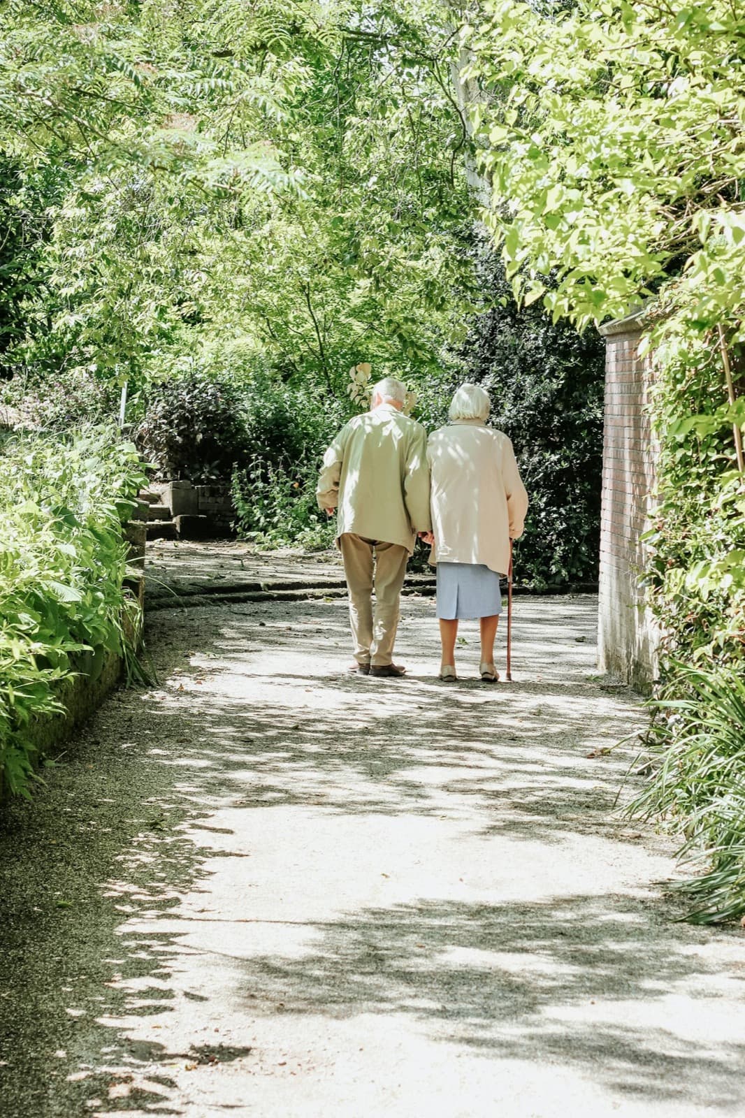 Two older adults walking together along a sunlit garden path
